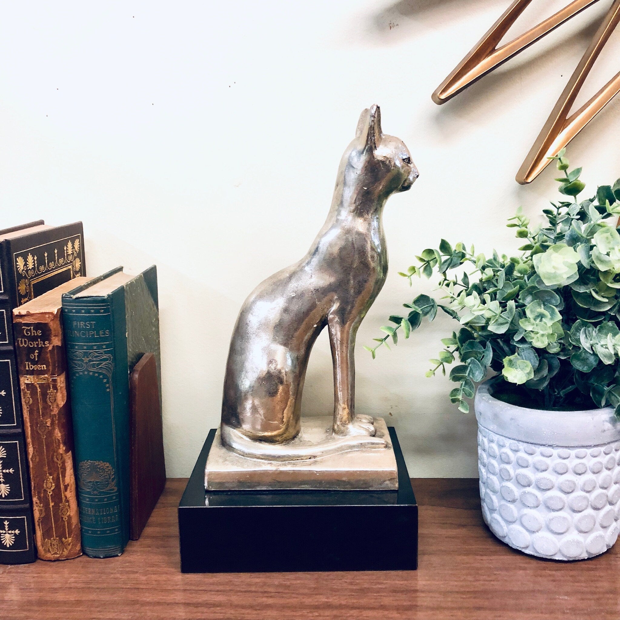 Silver cat statue on wooden base beside books and flower pot, vintage home decor