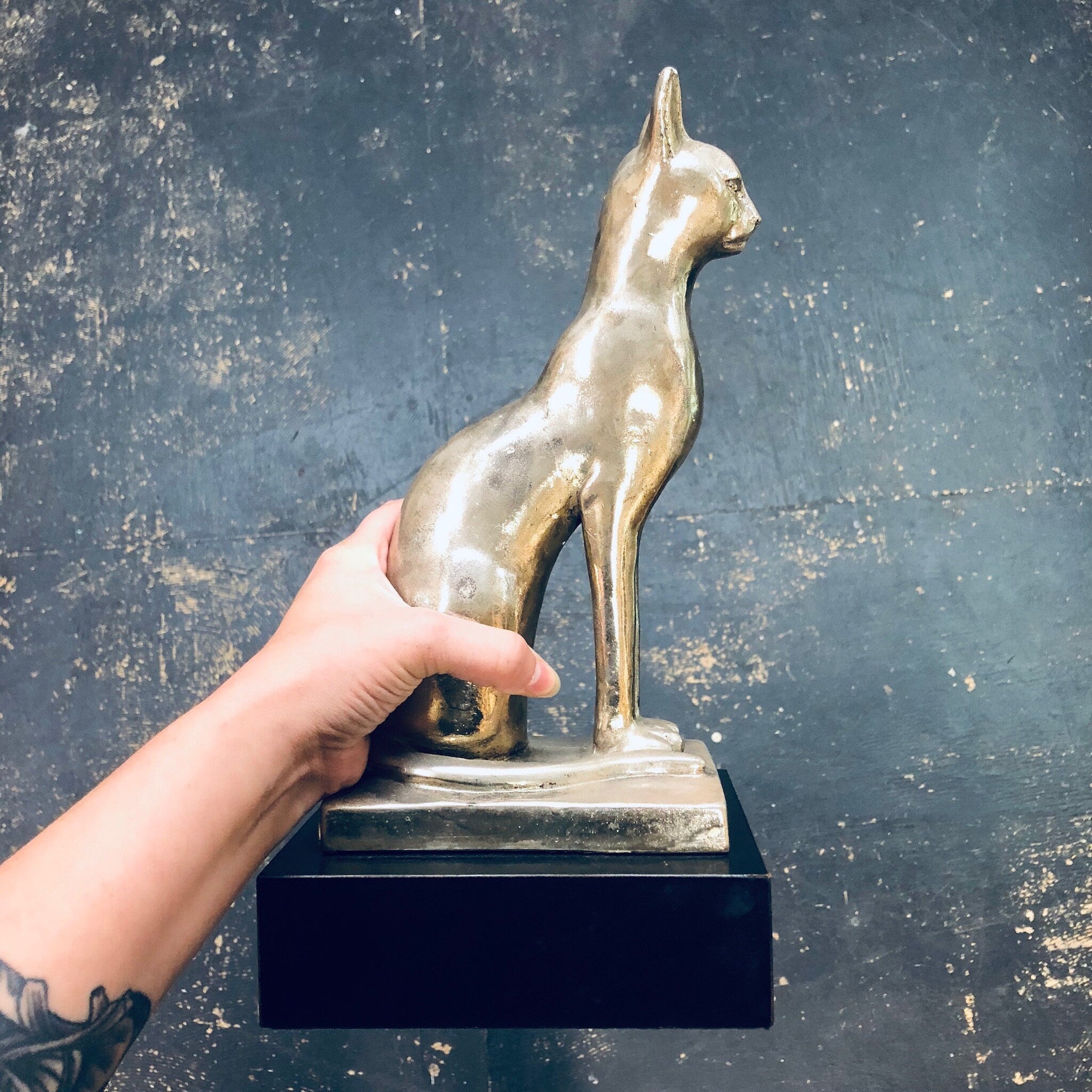 Hand holding vintage silver cat statue against dark textured background