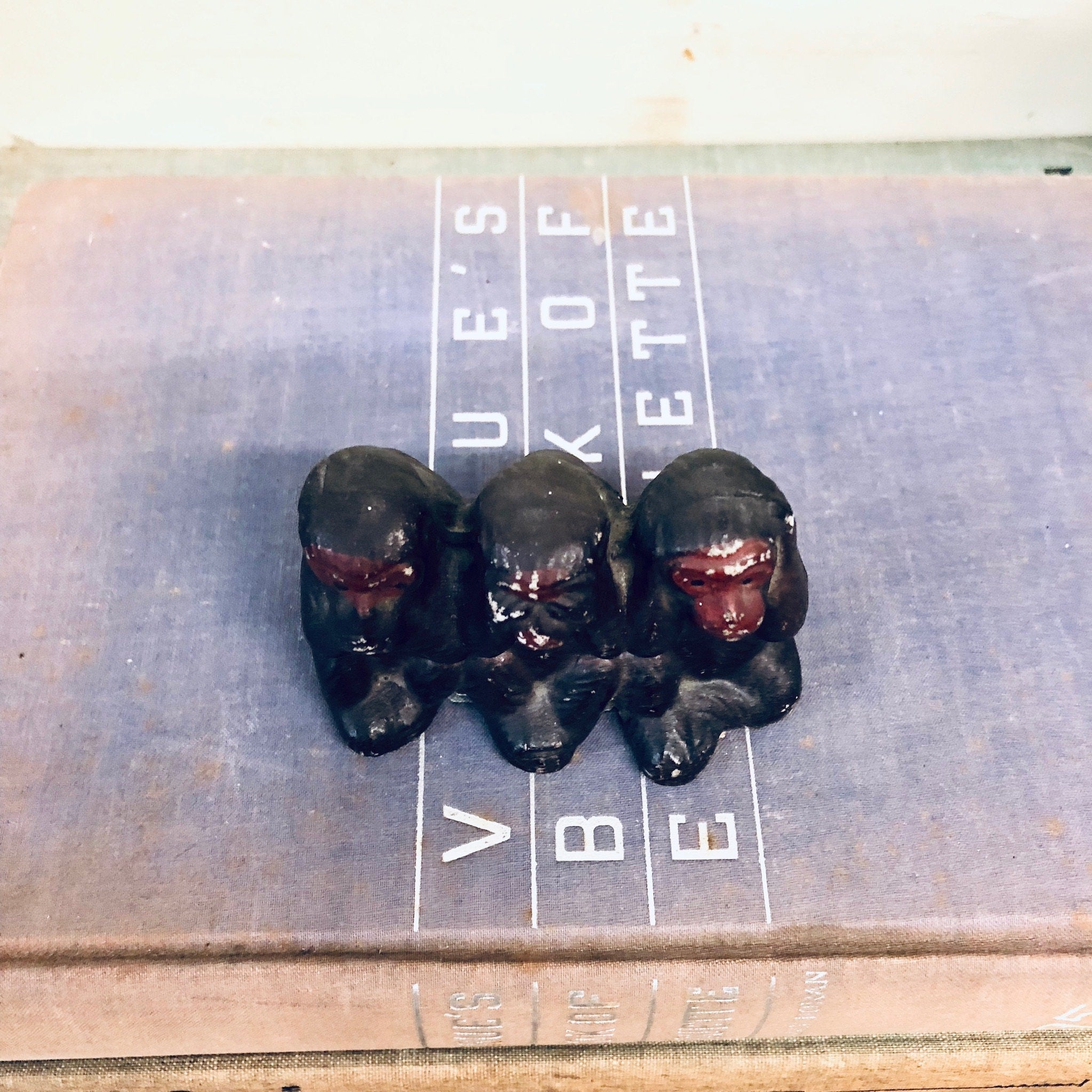 Three vintage ceramic monkey figurines depicting "see no evil, hear no evil, speak no evil" posed on a measuring scale.