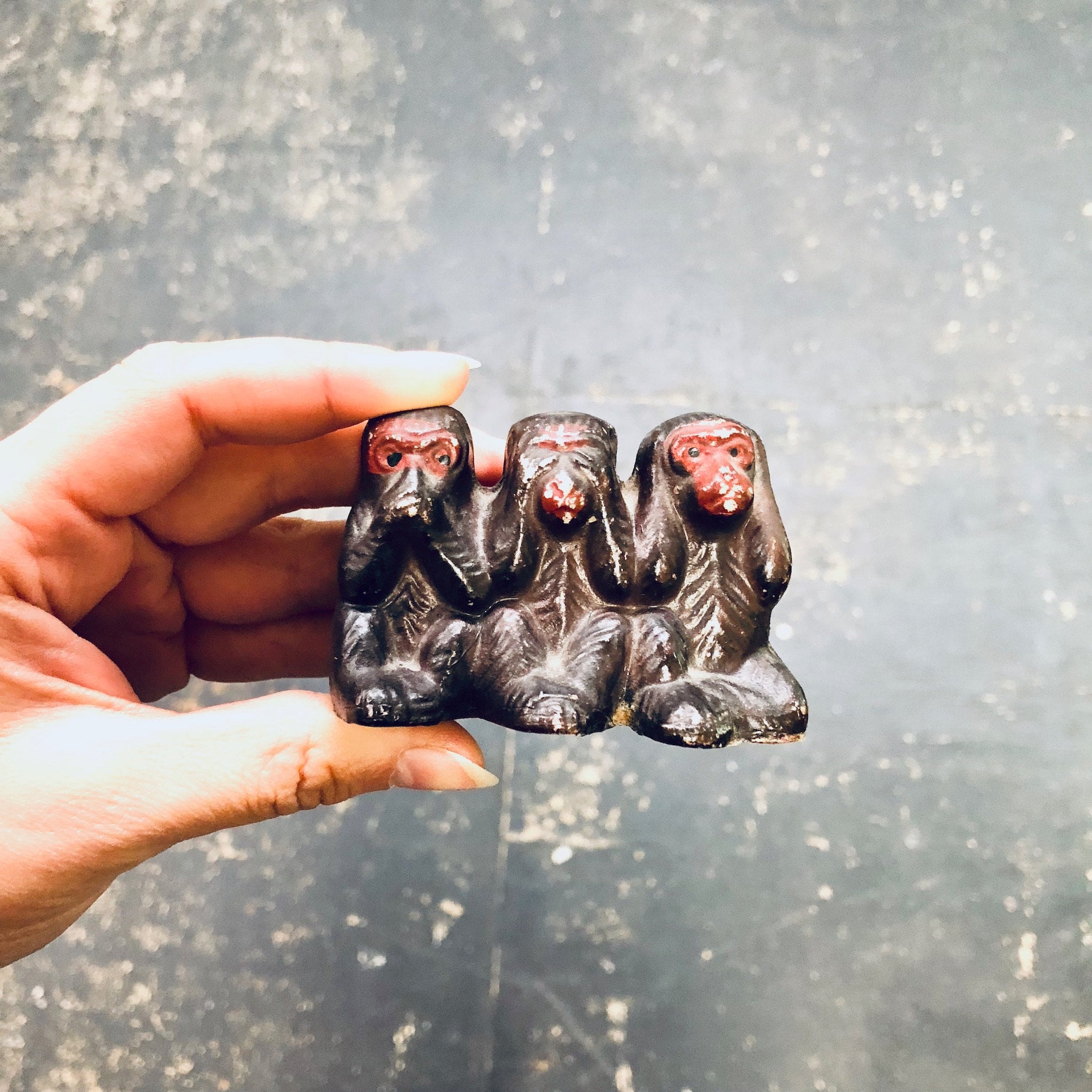 Three ceramic monkey figurines depicting "see no evil, hear no evil, speak no evil" on a reflective surface being held in a hand.