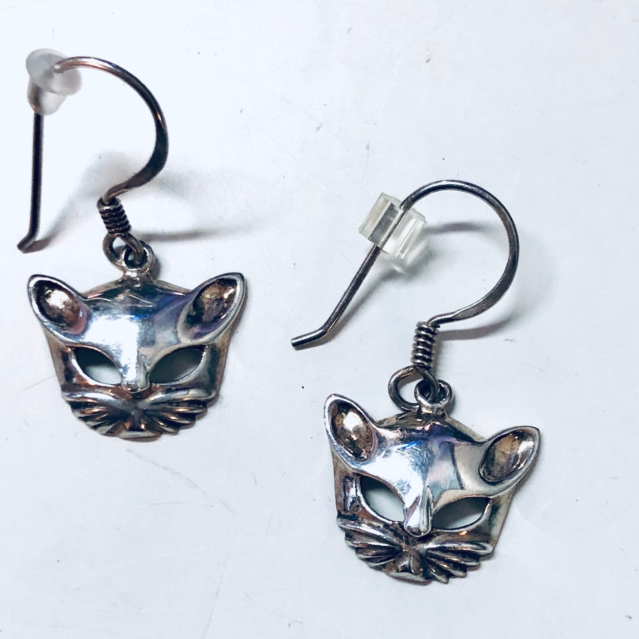 Silver cat mask dangle earrings featuring cut-out design depicting feline face with whiskers