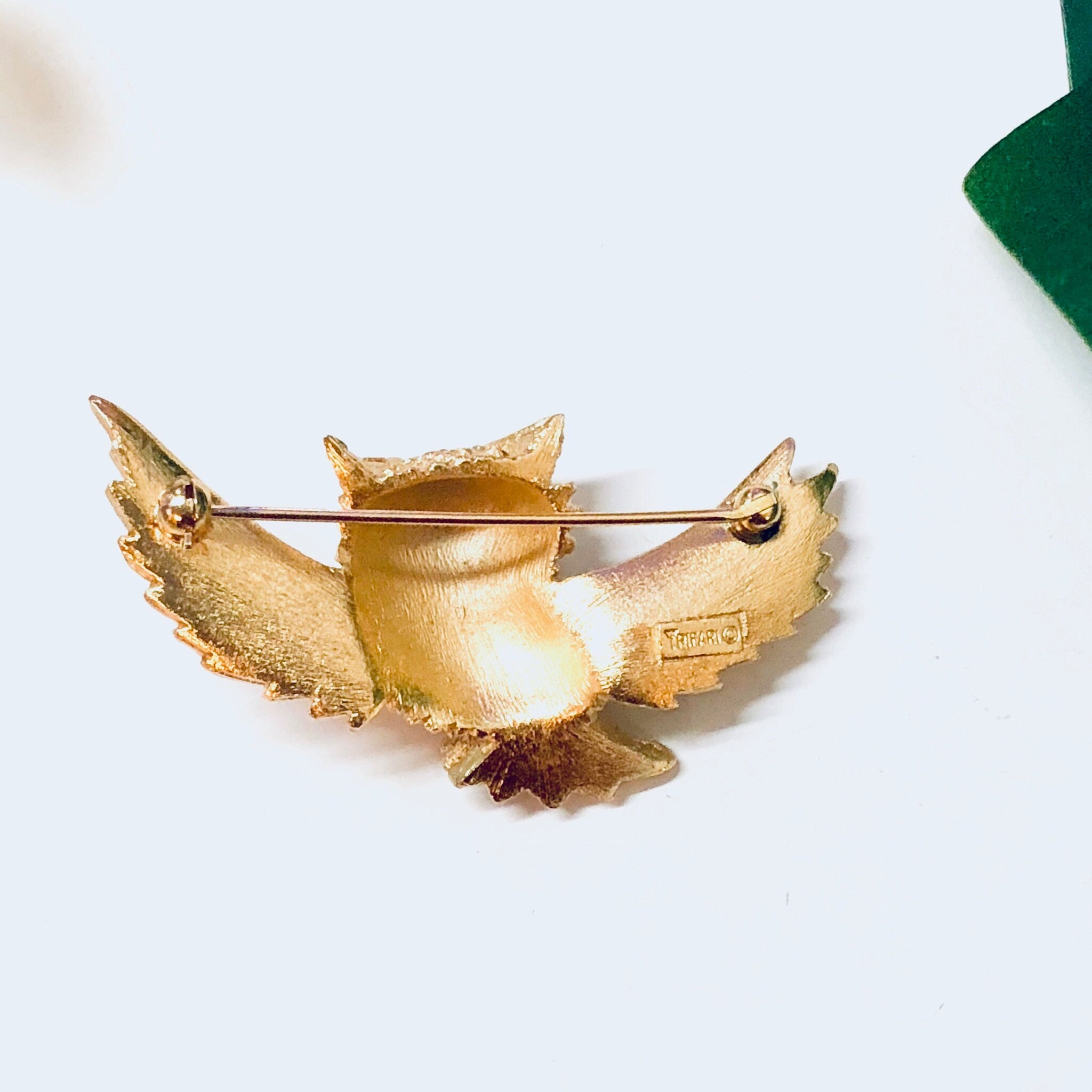 Vintage gold-toned Trifari owl brooch pin with detailed wings and textured surface, displayed on a white background with a green velvet accent.