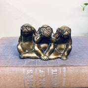 Three brass monkey figurines in "see no evil, hear no evil, speak no evil" poses on top of a book