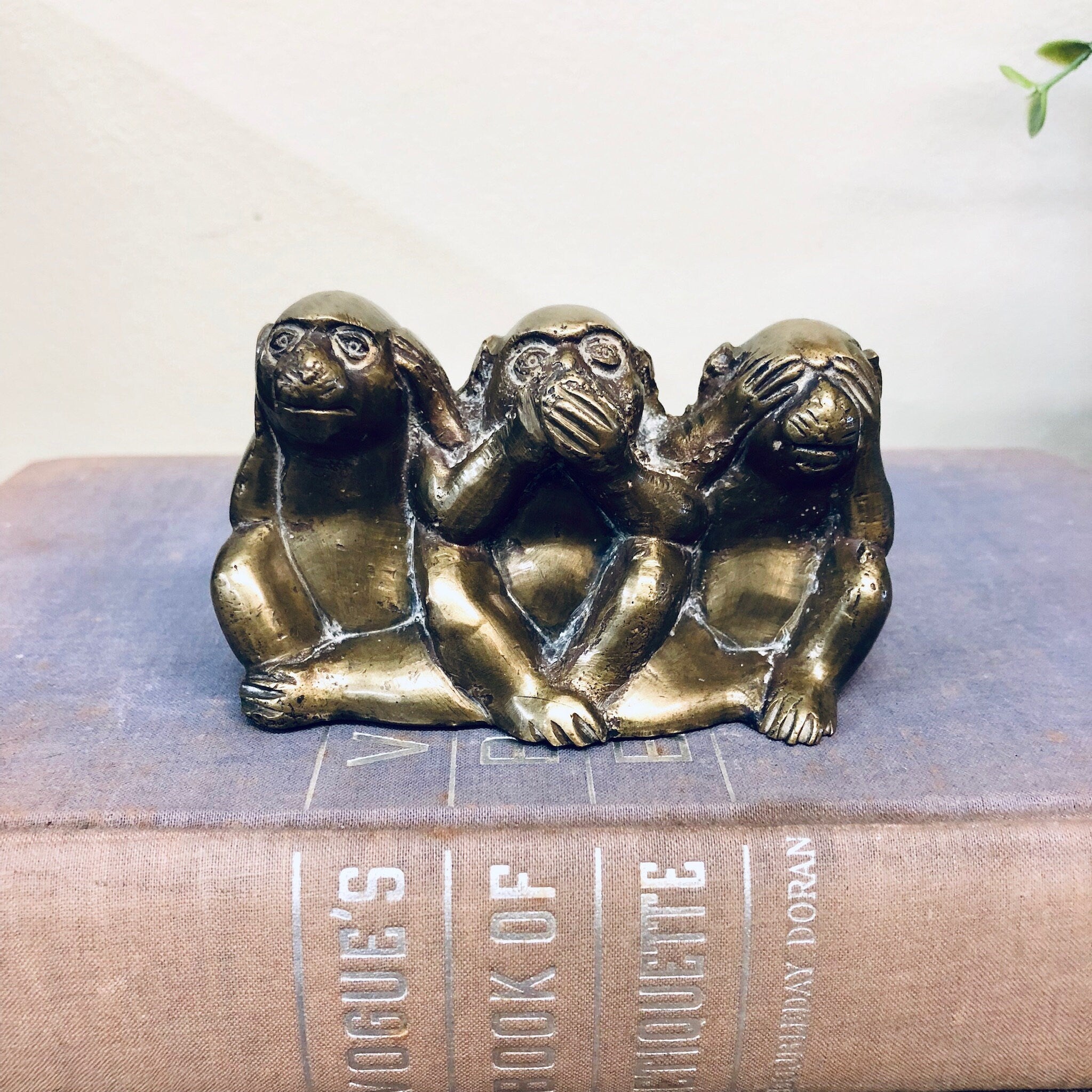 Three brass monkey figurines in "see no evil, hear no evil, speak no evil" poses on top of a book