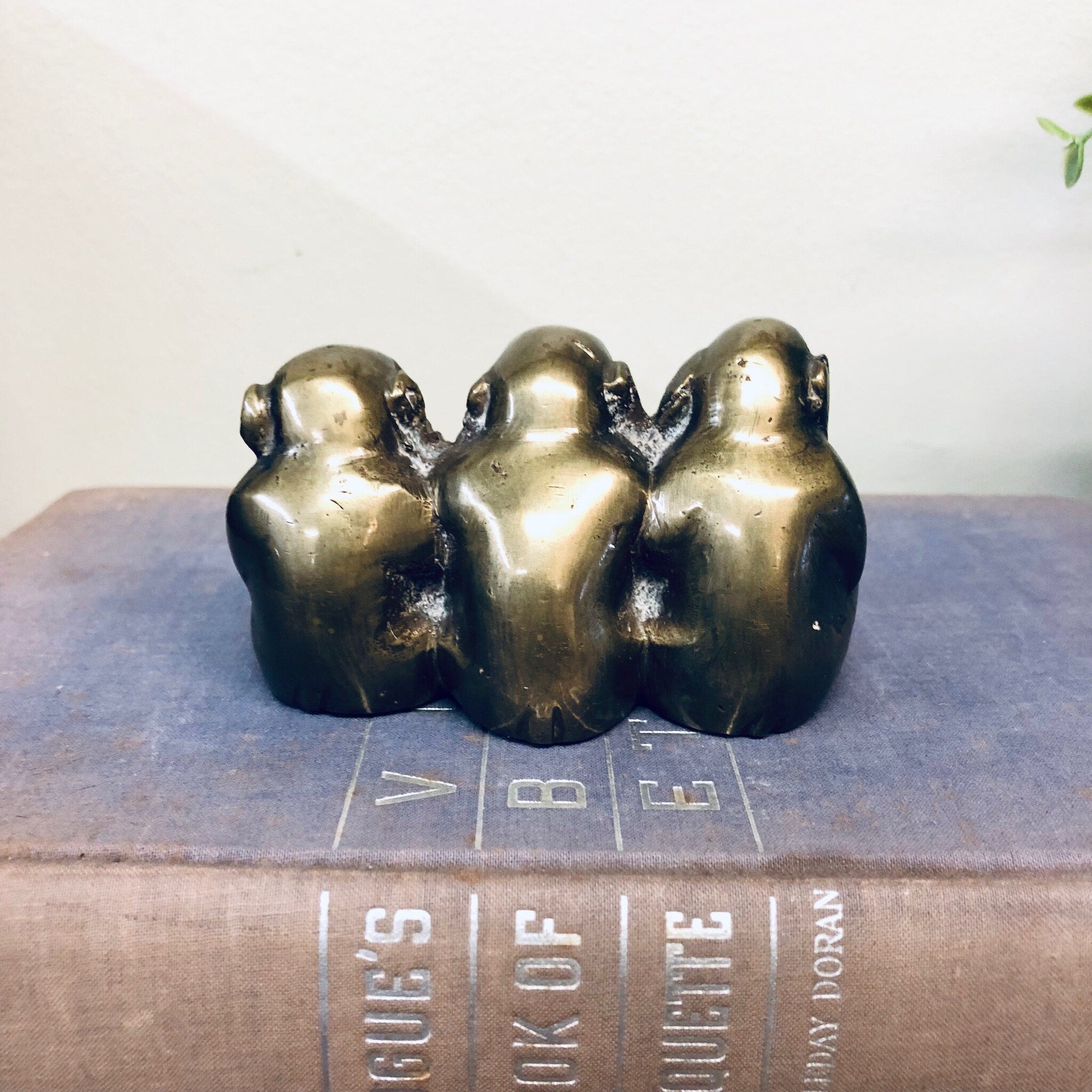 Three brass monkey figurines depicting "see no evil, hear no evil, speak no evil" on vintage book