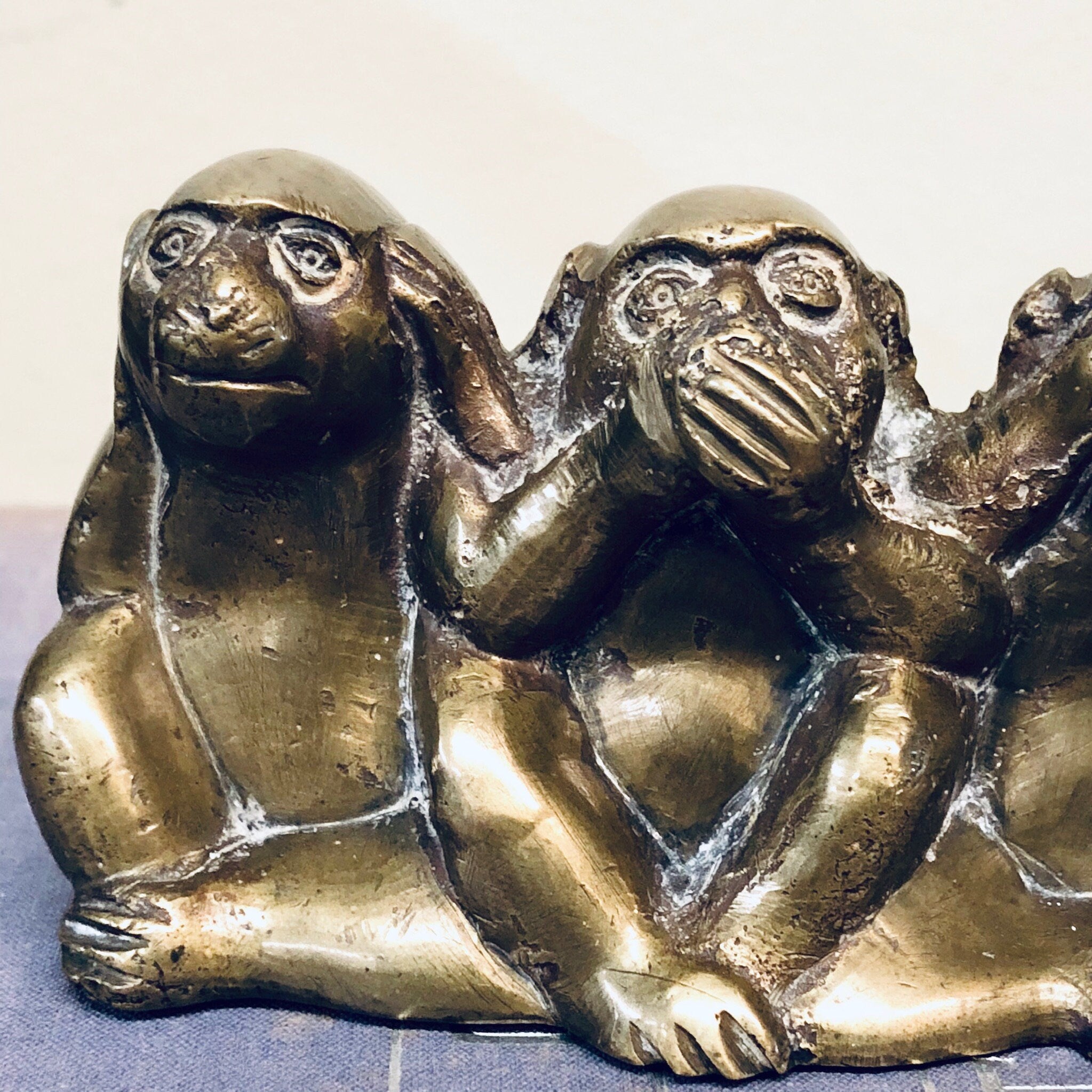 Three brass monkey figurines depicting "see no evil, hear no evil, speak no evil" proverb, sitting in poses with hands covering eyes, ears, and mouth, tarnished vintage home decor.