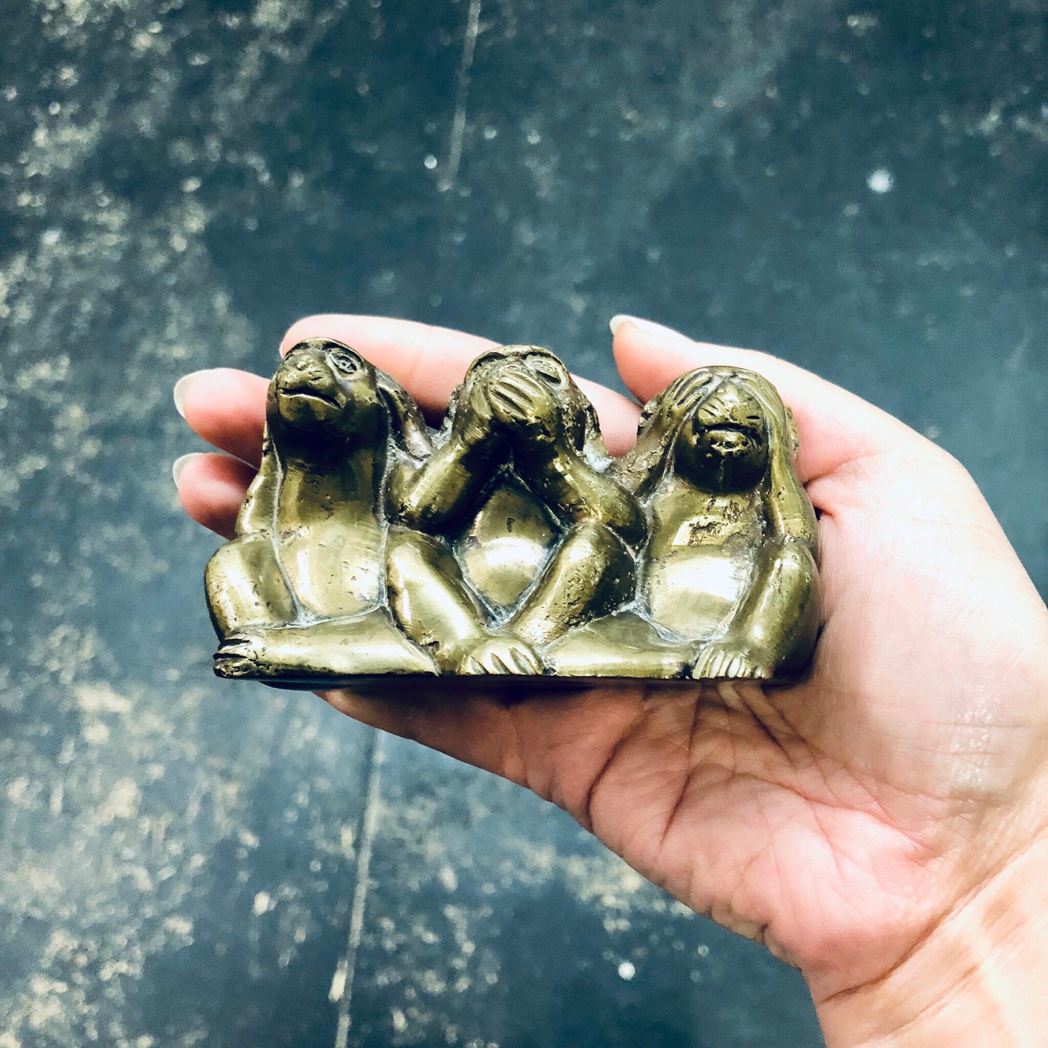 Three brass monkey figurines depicting "see no evil, hear no evil, speak no evil" held in a person's hand.