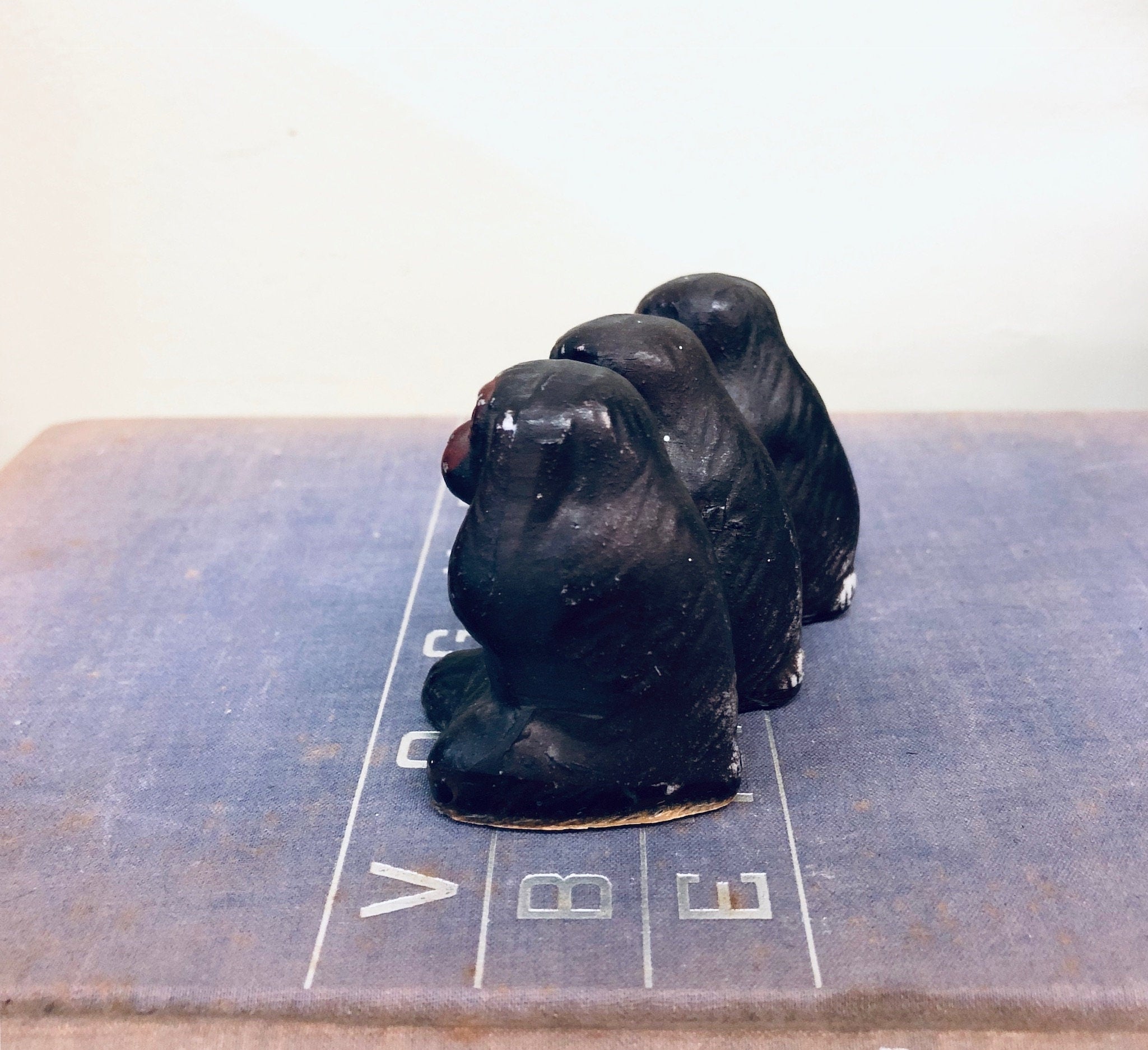 Three wise monkey figurines in black color sitting on a game board with "V B E" text, vintage Japanese home decor trinket