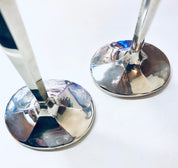 Pair of vintage sterling silver candle holders with curved bases reflecting light, holding white tapered candles against a white background.