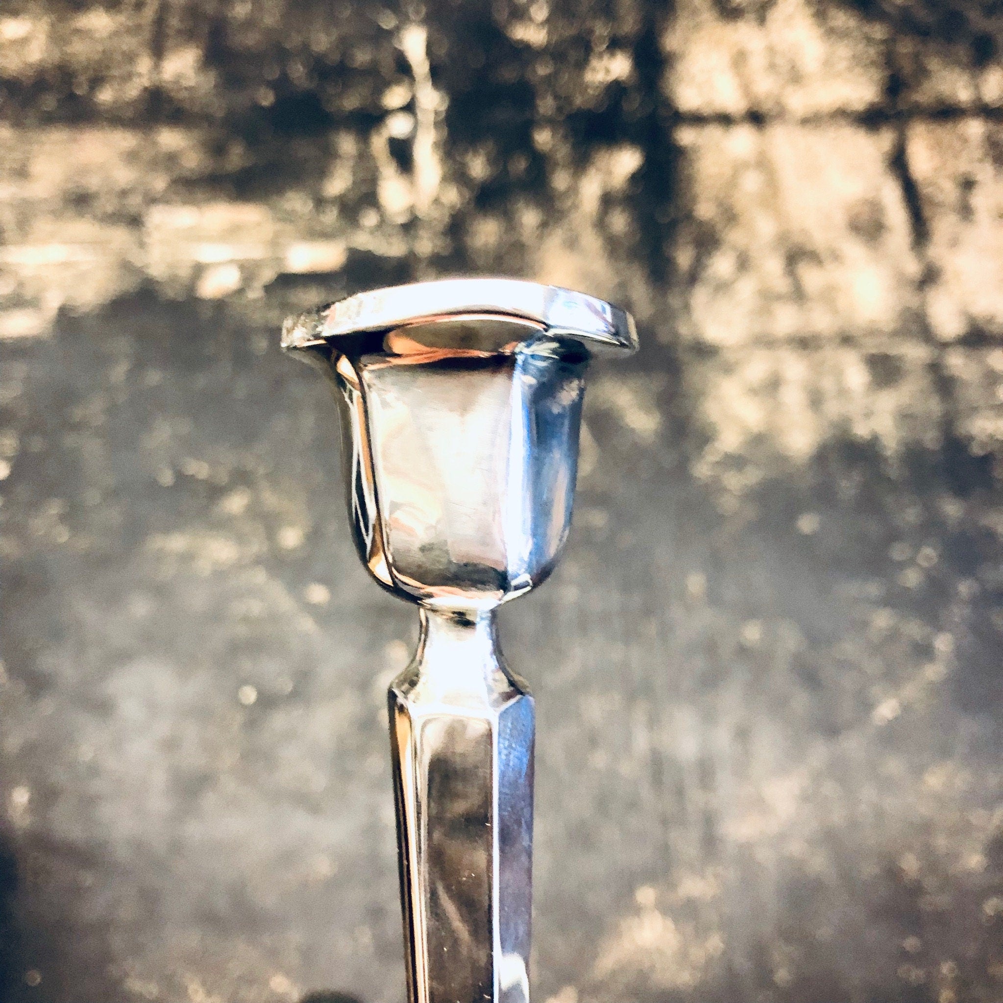 Vintage silver candlestick holder with a polished, shiny finish, photographed against an aged, textured background.