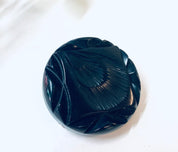 Black carved Bakelite mourning brooch from the 1930s, featuring a round design with intricate etched details on the vintage pin.