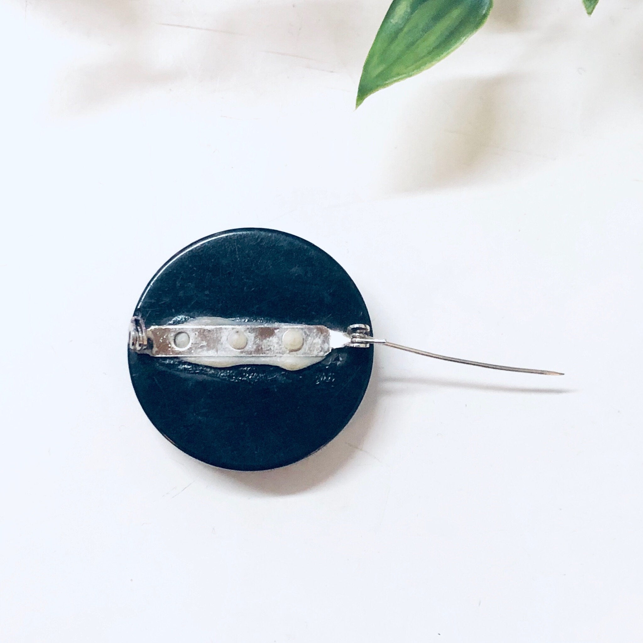 Black bakelite vintage mourning brooch pinned against white fabric with green leaf in background