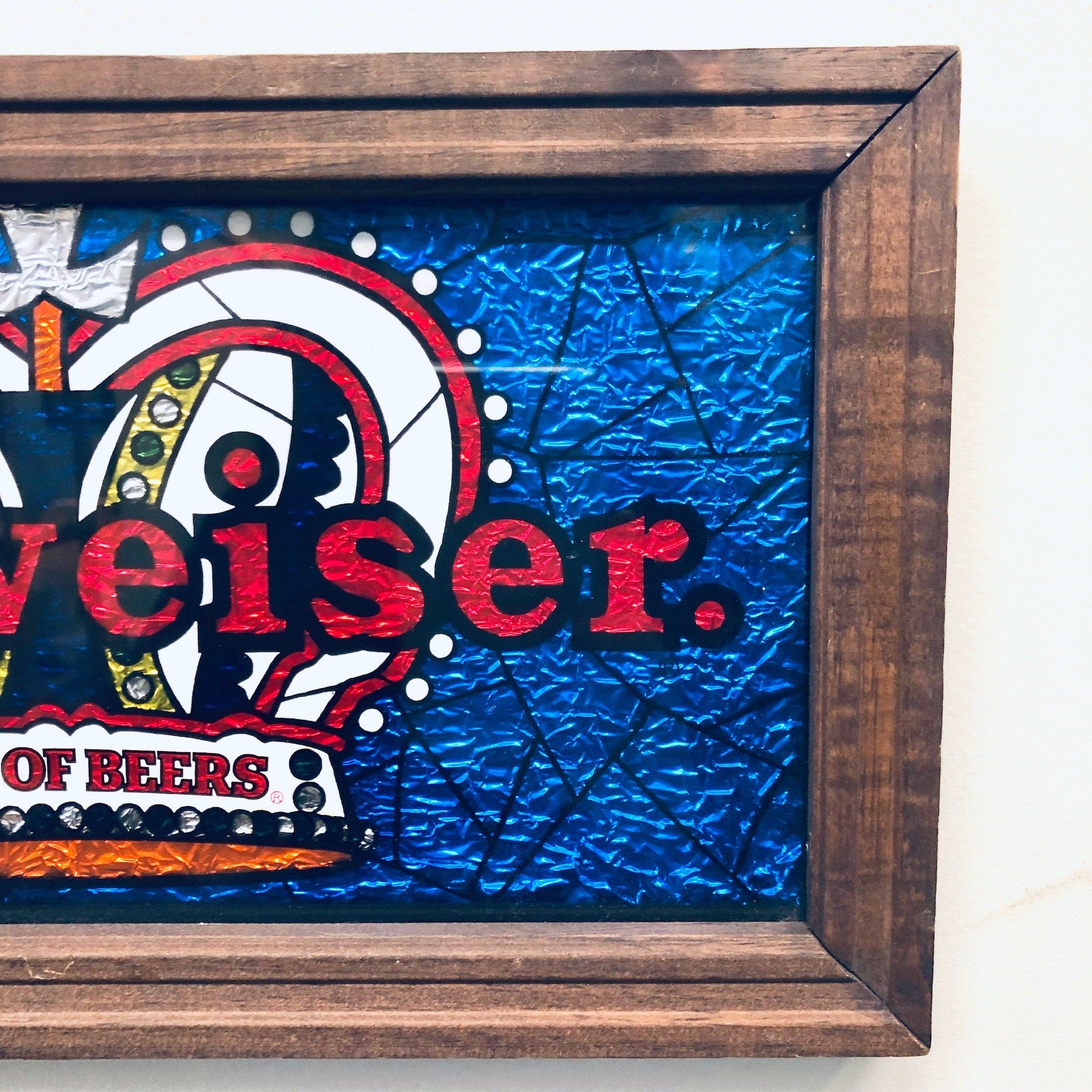 Vintage Budweiser beer sign with red text and dart board design, framed in rustic wood, mounted on textured blue background.