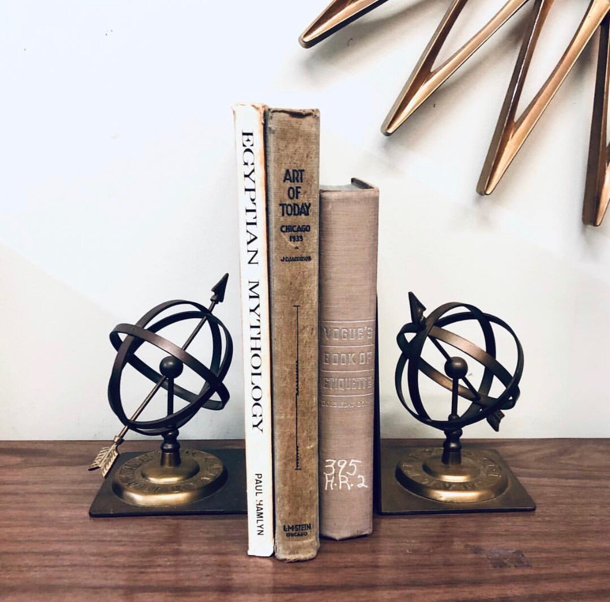 Vintage brass spherical sundial bookends with Roman numerals on a wooden shelf, surrounded by antique books. Unique home decor for a bookshelf or library.