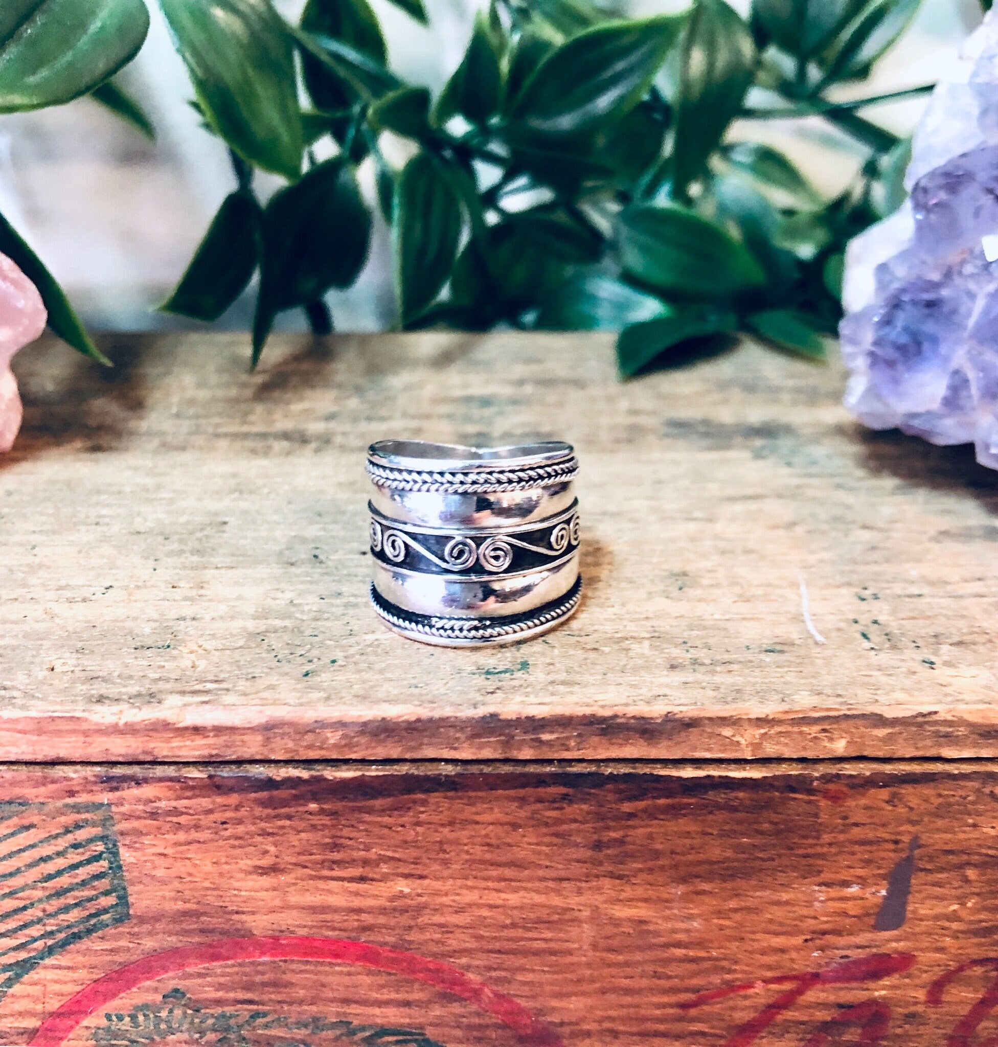 Vintage silver swirl design band ring on wooden surface with plants in background