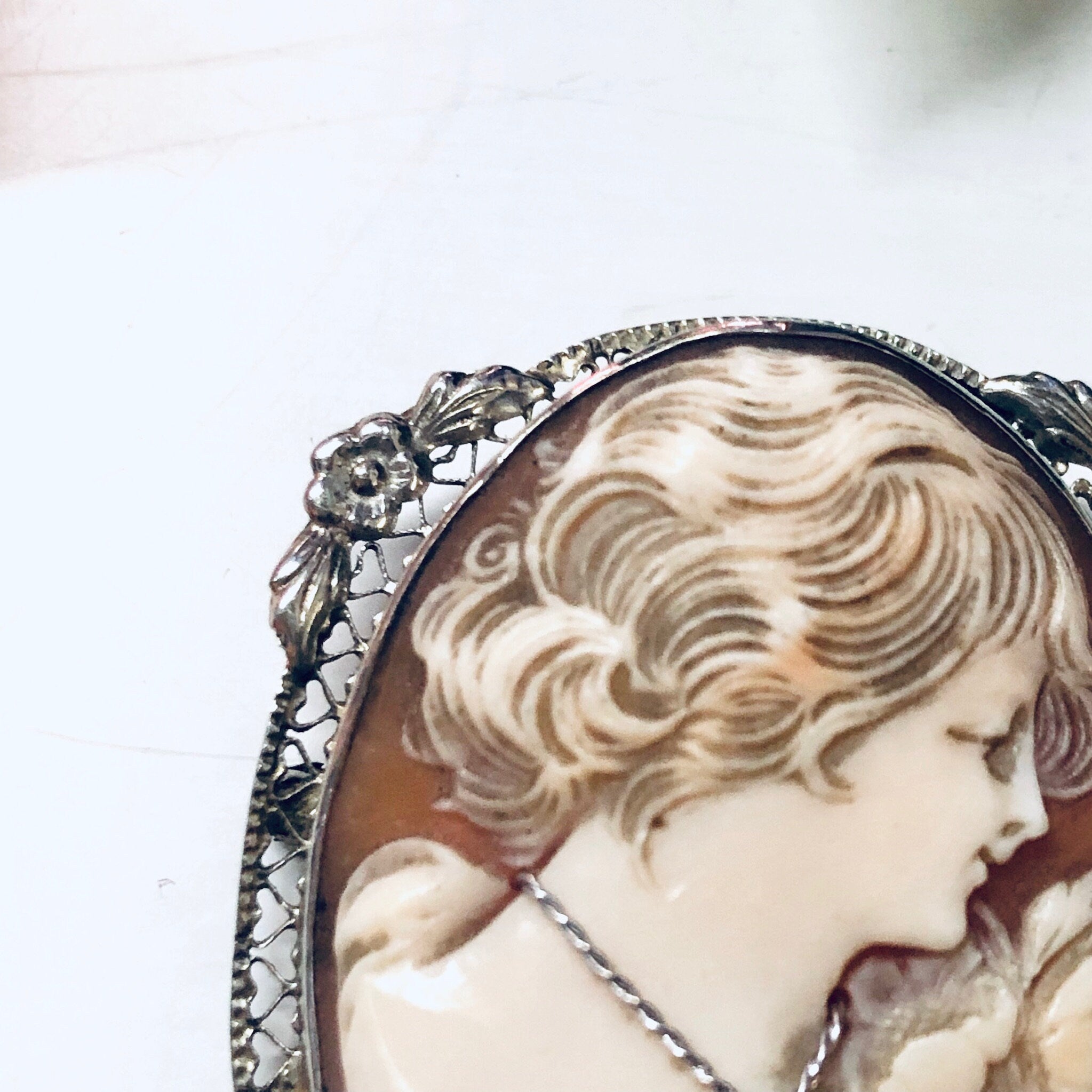 Antique cameo brooch featuring an intricate profile portrait carved in shell, set in an ornate 18K white gold frame with detailed scrollwork and floral designs. The cameo depicts a serene woman's face in a classical Victorian style.