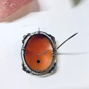 Vintage 18K white gold cameo brooch pendant featuring an ornate frame and burnt orange shell cameo against a white background.