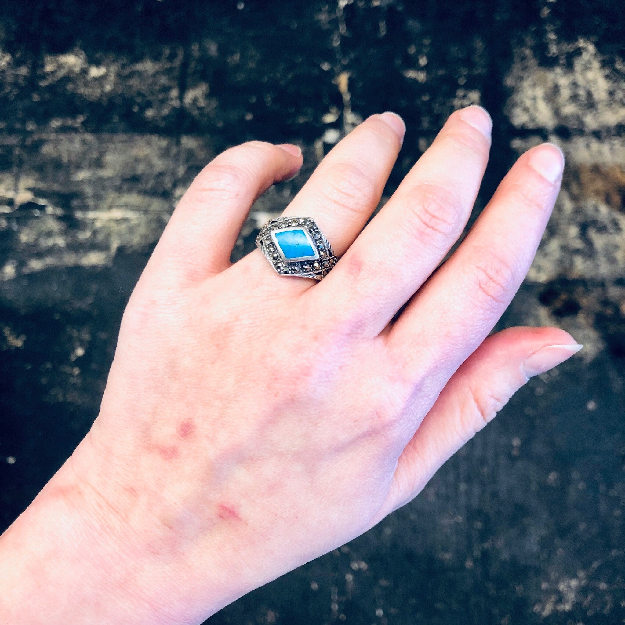 Vintage silver and turquoise marcasite ring on a hand, showcasing the diamond-shaped design with blue stone and sparkly 925 silver band, against a dark background.