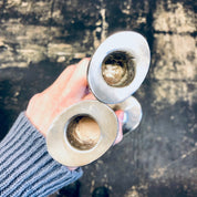 Two hands holding vintage silver candlesticks on a weathered surface, with the candlesticks reflecting light.