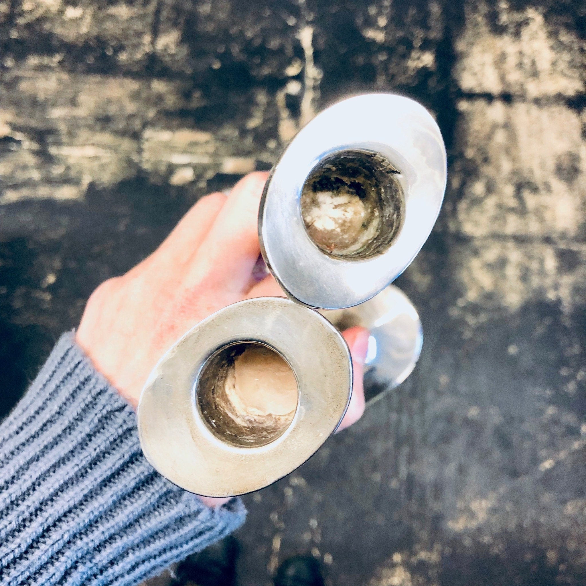 Two hands holding vintage silver candlesticks on a weathered surface, with the candlesticks reflecting light.