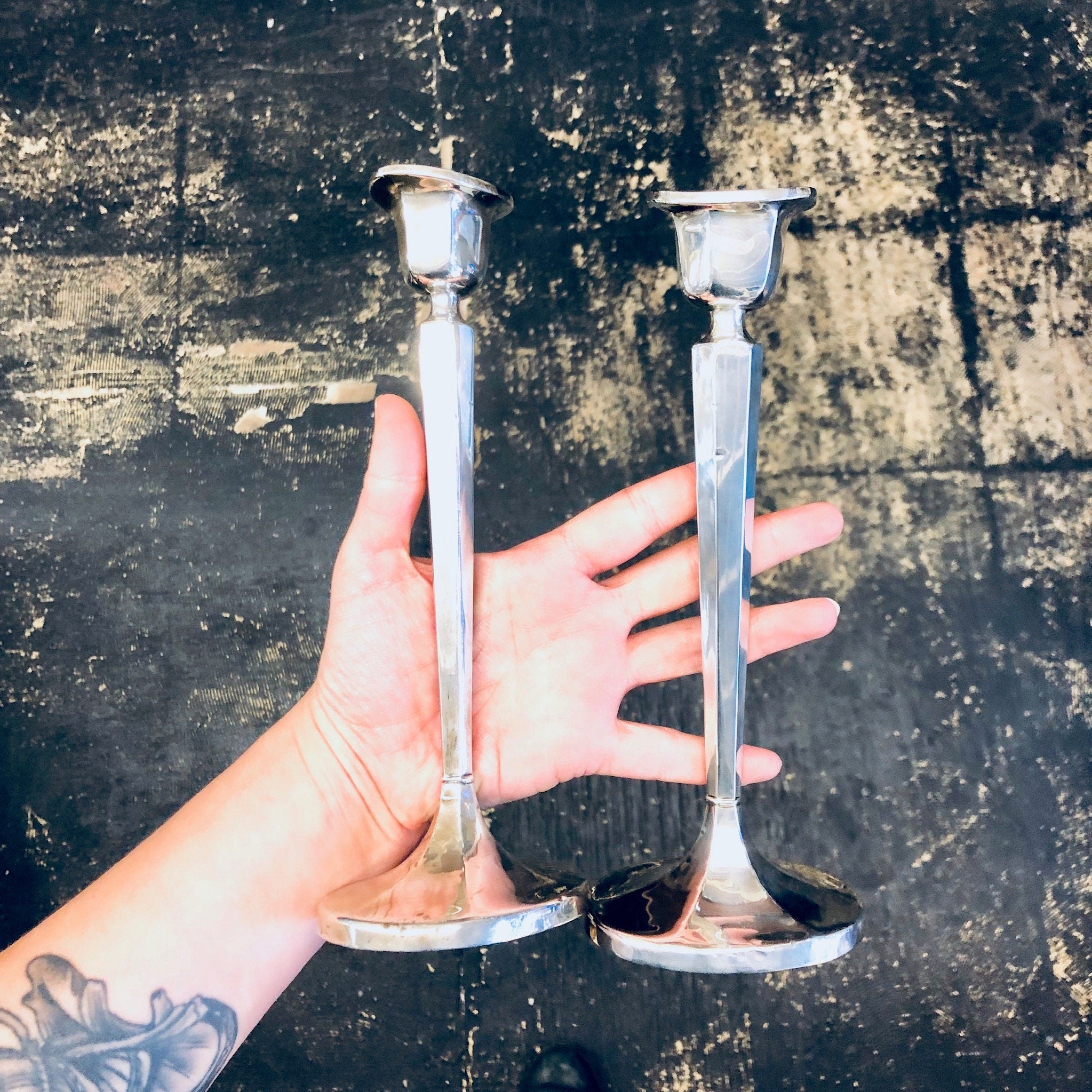 A hand holding two vintage silver candlesticks against a grungy background.