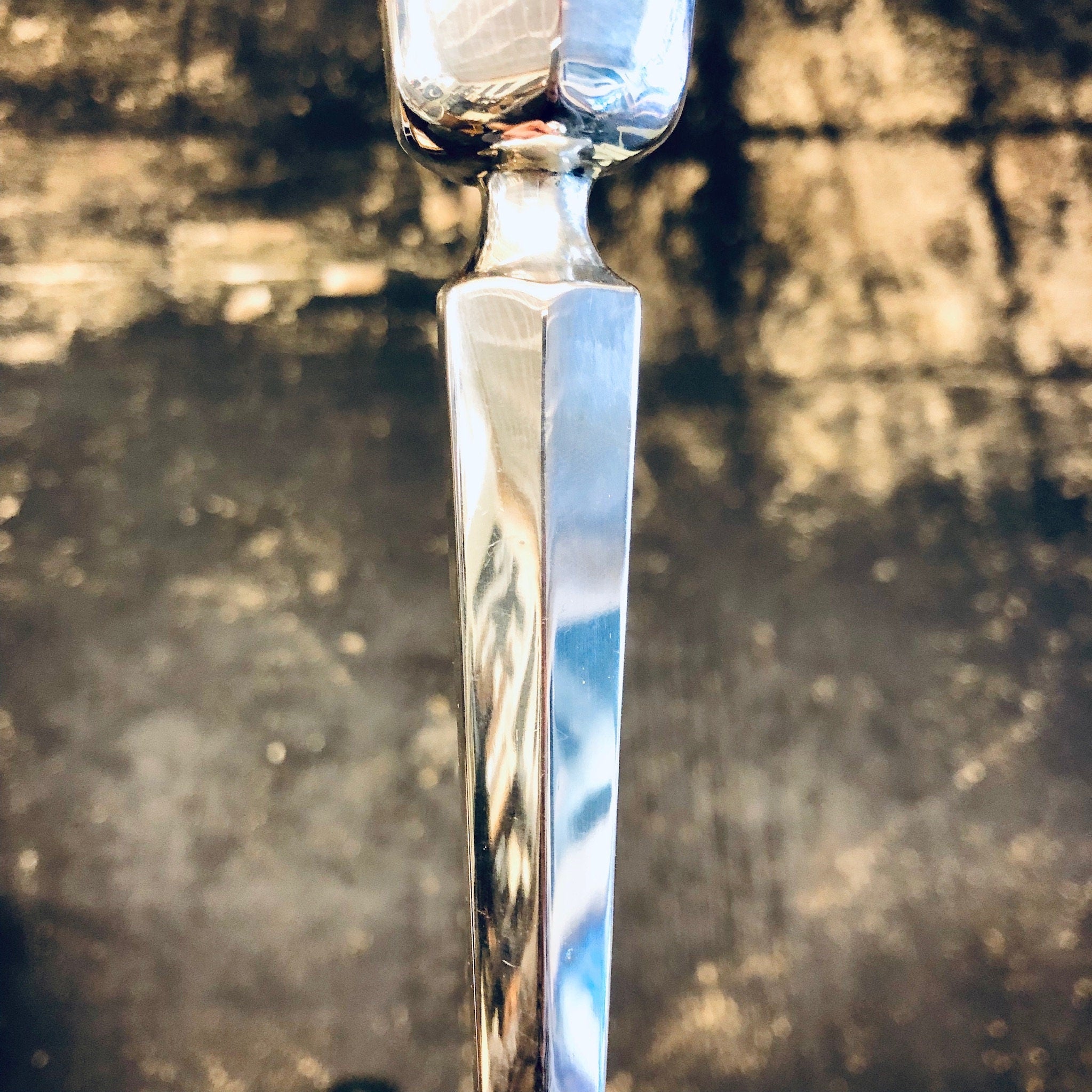 Vintage silver candlestick with ornate details catching the sunlight against a blurred stone background