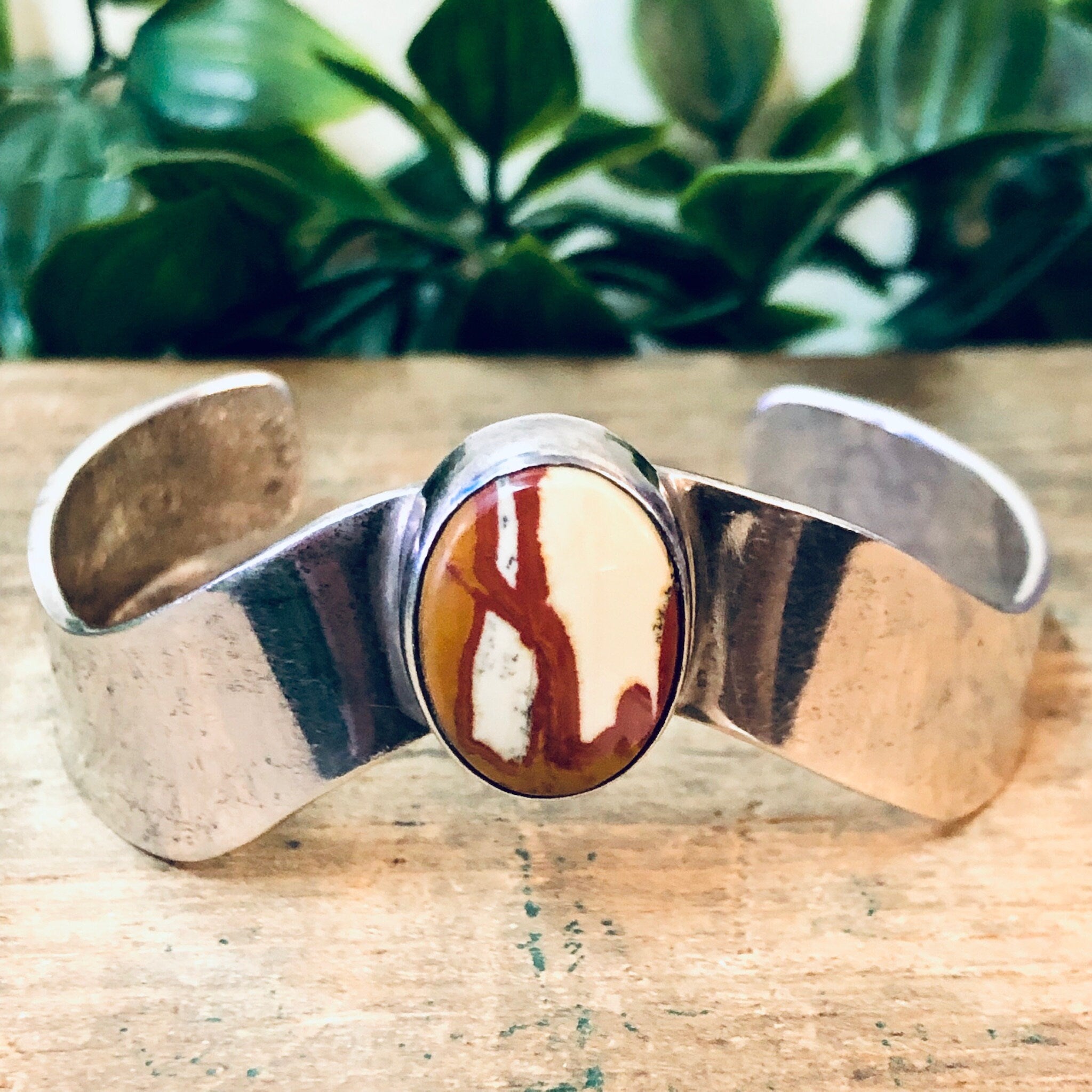 Vintage silver cuff bracelet with red natural stone inlay, set against a wooden surface with greenery in the background.