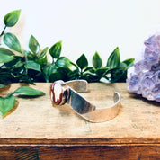 Vintage silver cuff bracelet with red natural stone on wooden surface with green leaves and amethyst crystal in background