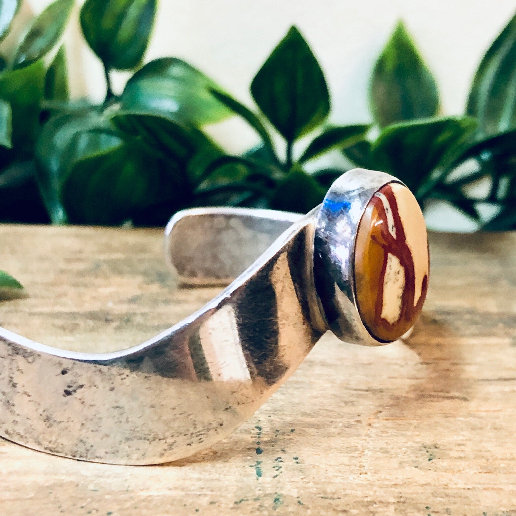 Vintage silver cuff bracelet with red and blue natural stone inlay, displayed on wooden surface with green foliage in background.