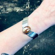 The image shows a vintage silver cuff bracelet with a red natural stone inlay worn on a person's wrist against an aged, weathered background.