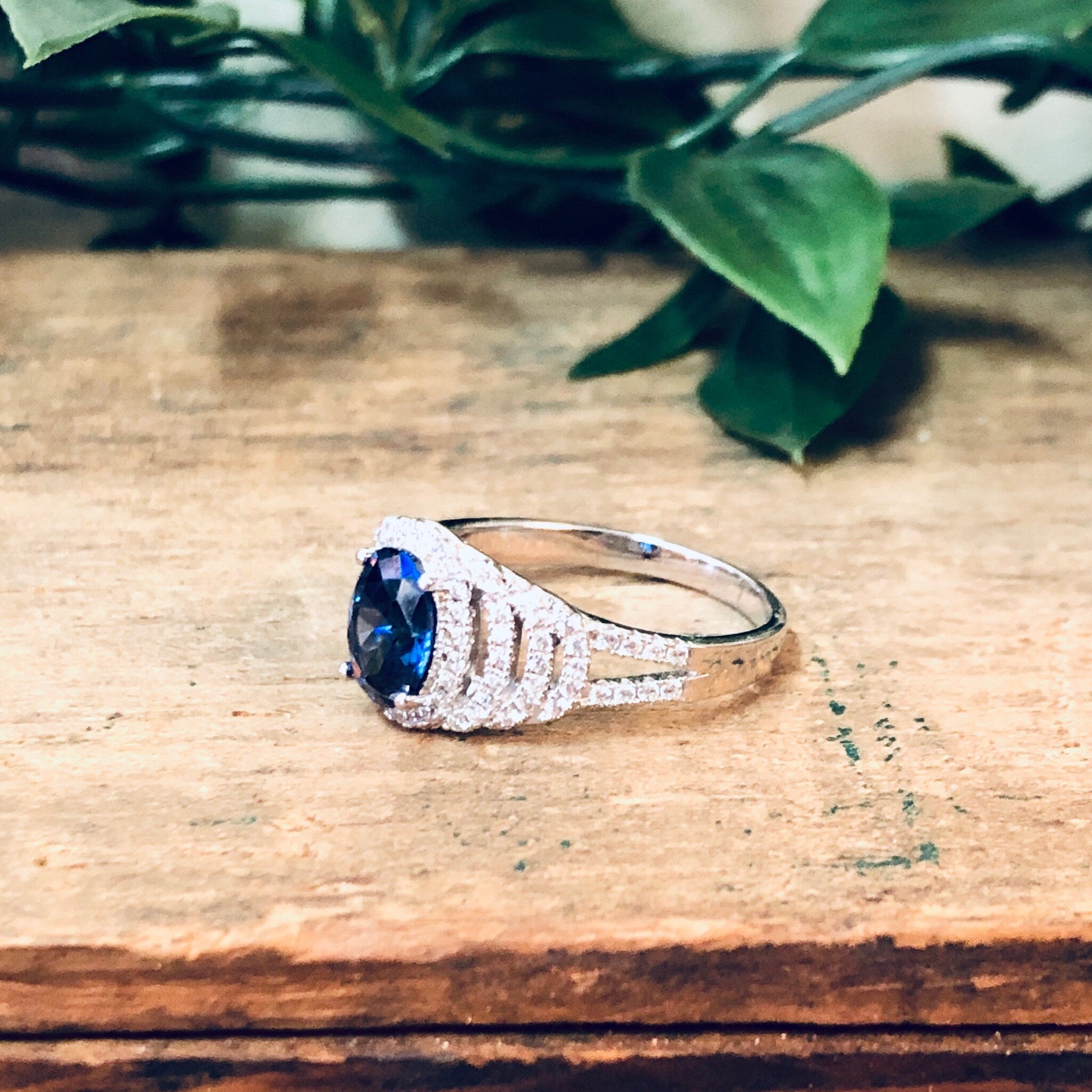 Vintage silver ring with blue stone and faux diamonds on wooden surface with green foliage in background