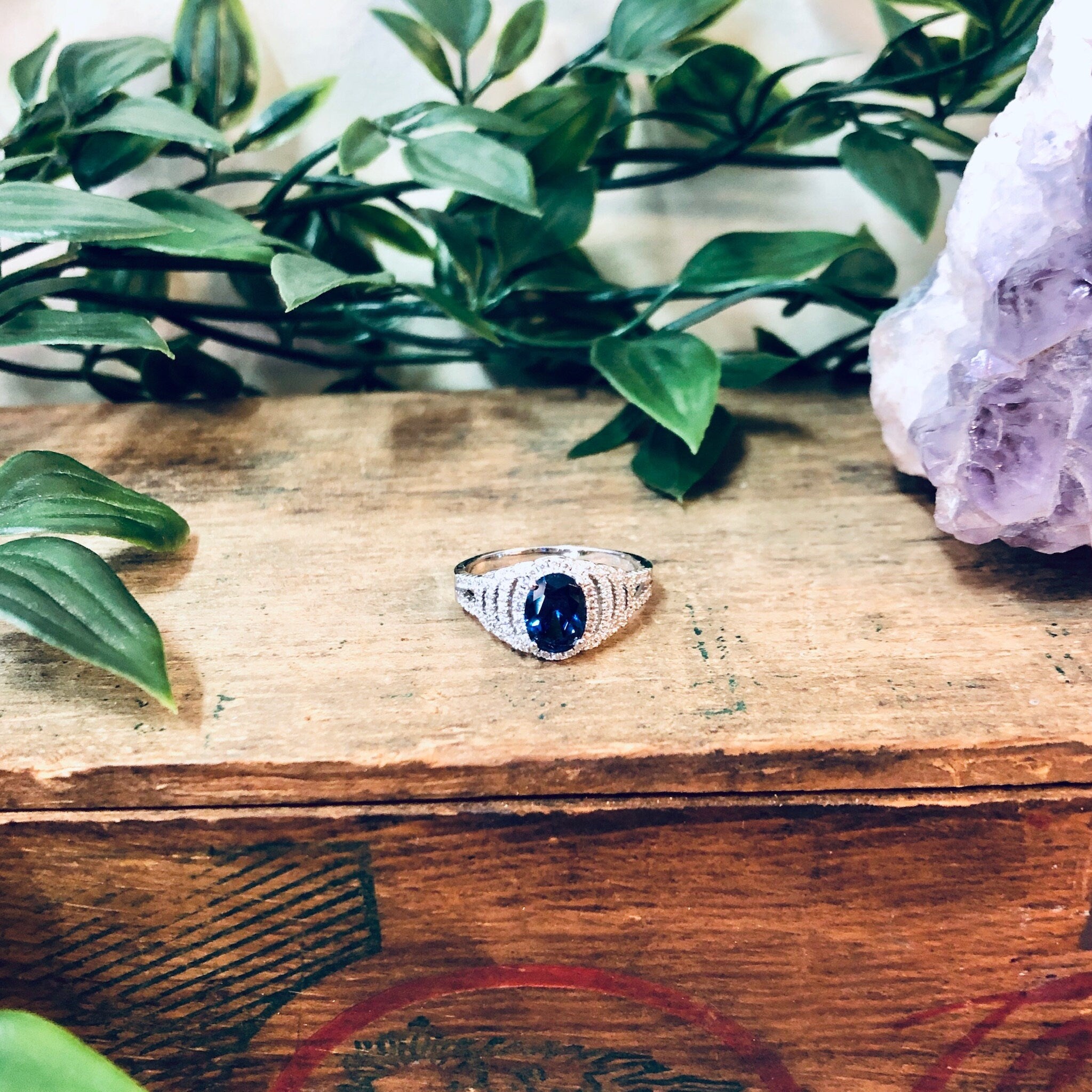 Vintage silver ring with blue stone on wooden surface surrounded by green leaves and amethyst crystal