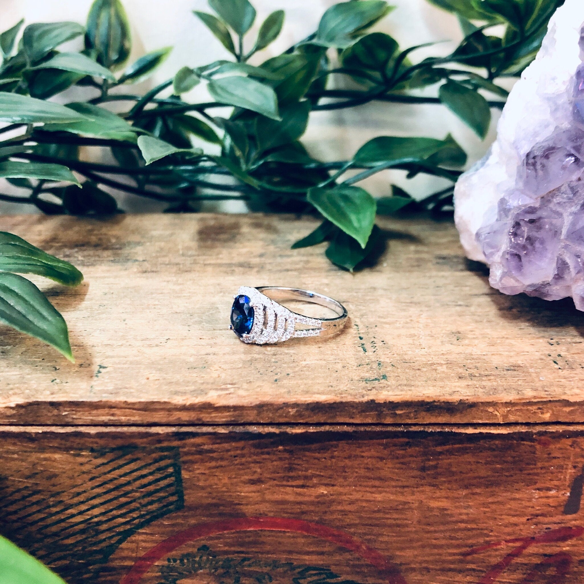 Vintage silver ring with blue stone on wooden surface surrounded by greenery