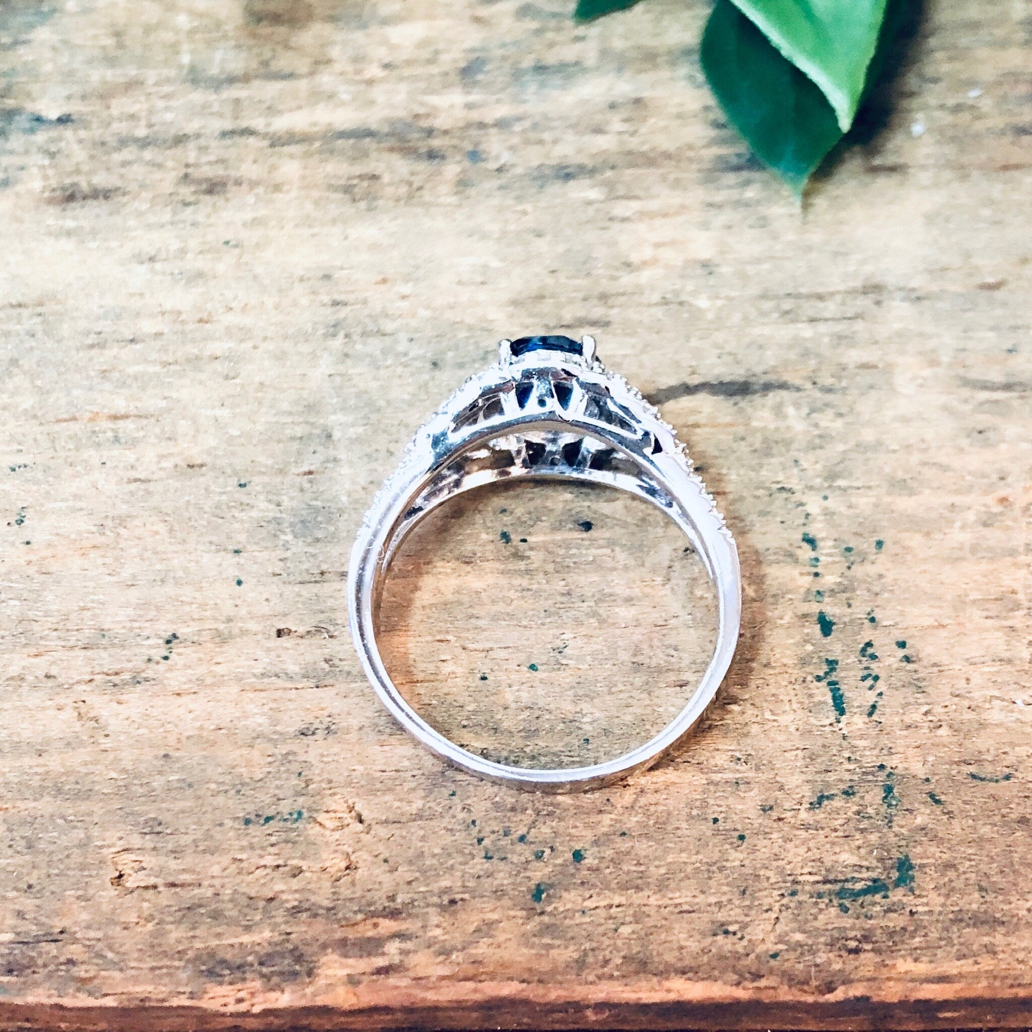 Vintage silver ring with blue stone and faux diamonds on wooden surface with green leaf
