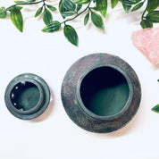 Vintage green ceramic incense burner with floral design and lid, surrounded by greenery and pink stones, unique housewarming gift idea.