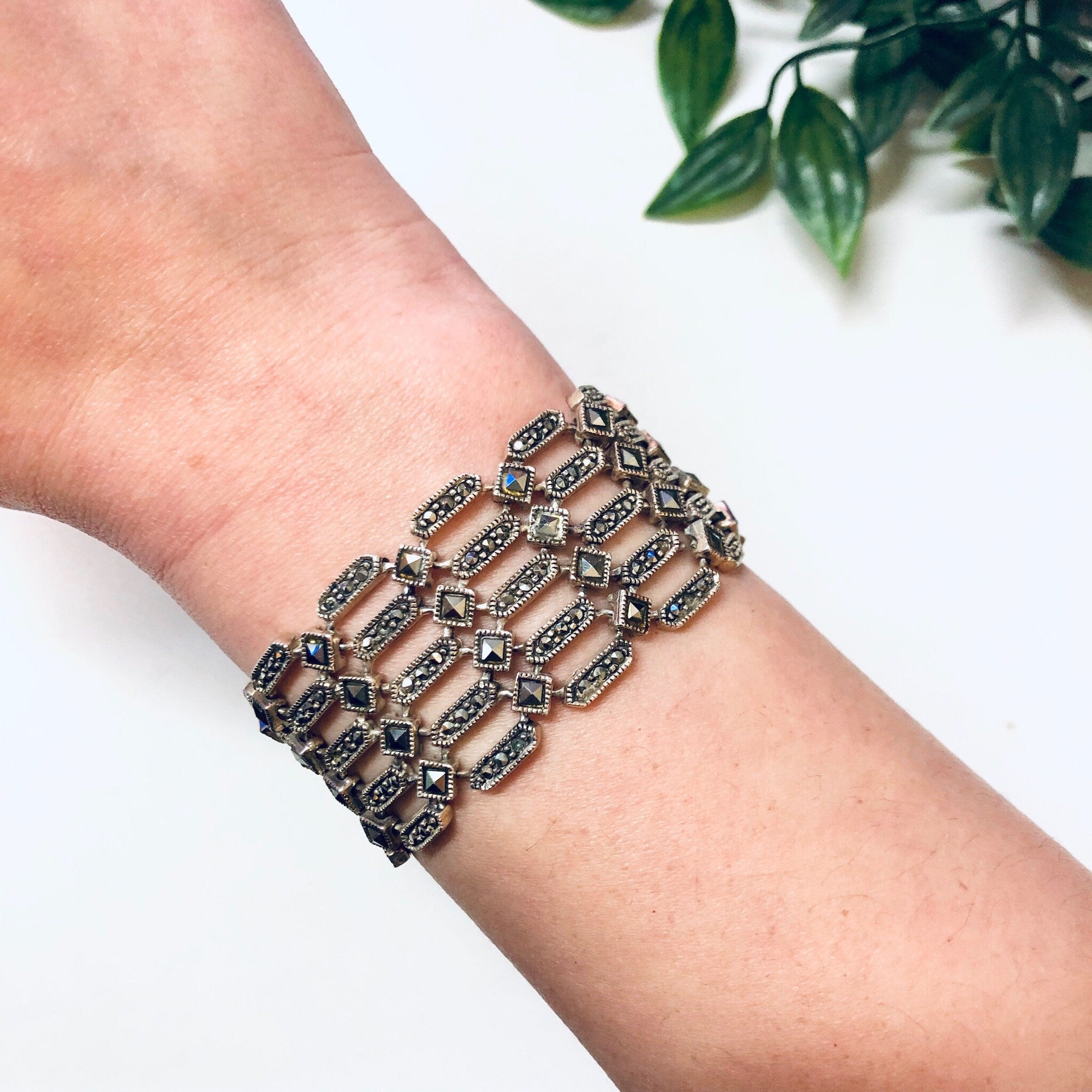 Vintage sterling silver marcasite link bracelet on wrist near green leaves, statement jewelry for Valentine's Day gift
