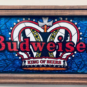 Vintage Budweiser beer sign with red and blue stained glass design featuring two rams and a crown, framed in wood with "King of Beers" text below the graphic.