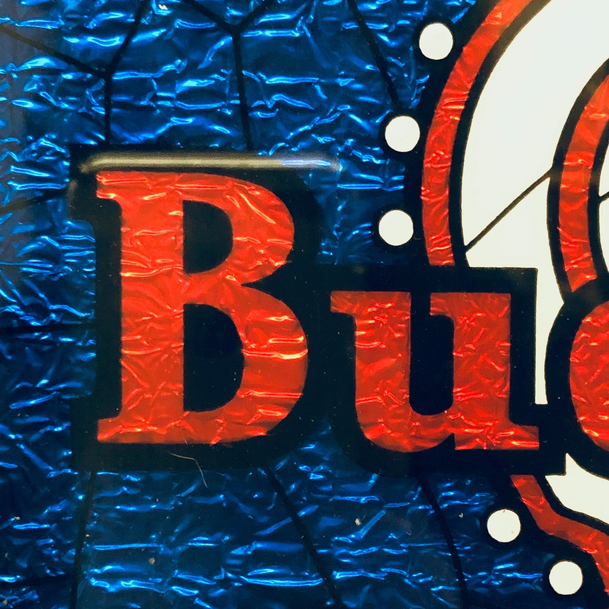 Vintage Budweiser beer sign with large red "Bu" letters on a textured blue background, framed in a white circular border and wood frame.