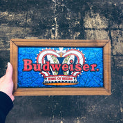 Vintage Budweiser "King of Beers" sign in blue and red, displayed in a wooden frame against a grungy wall.