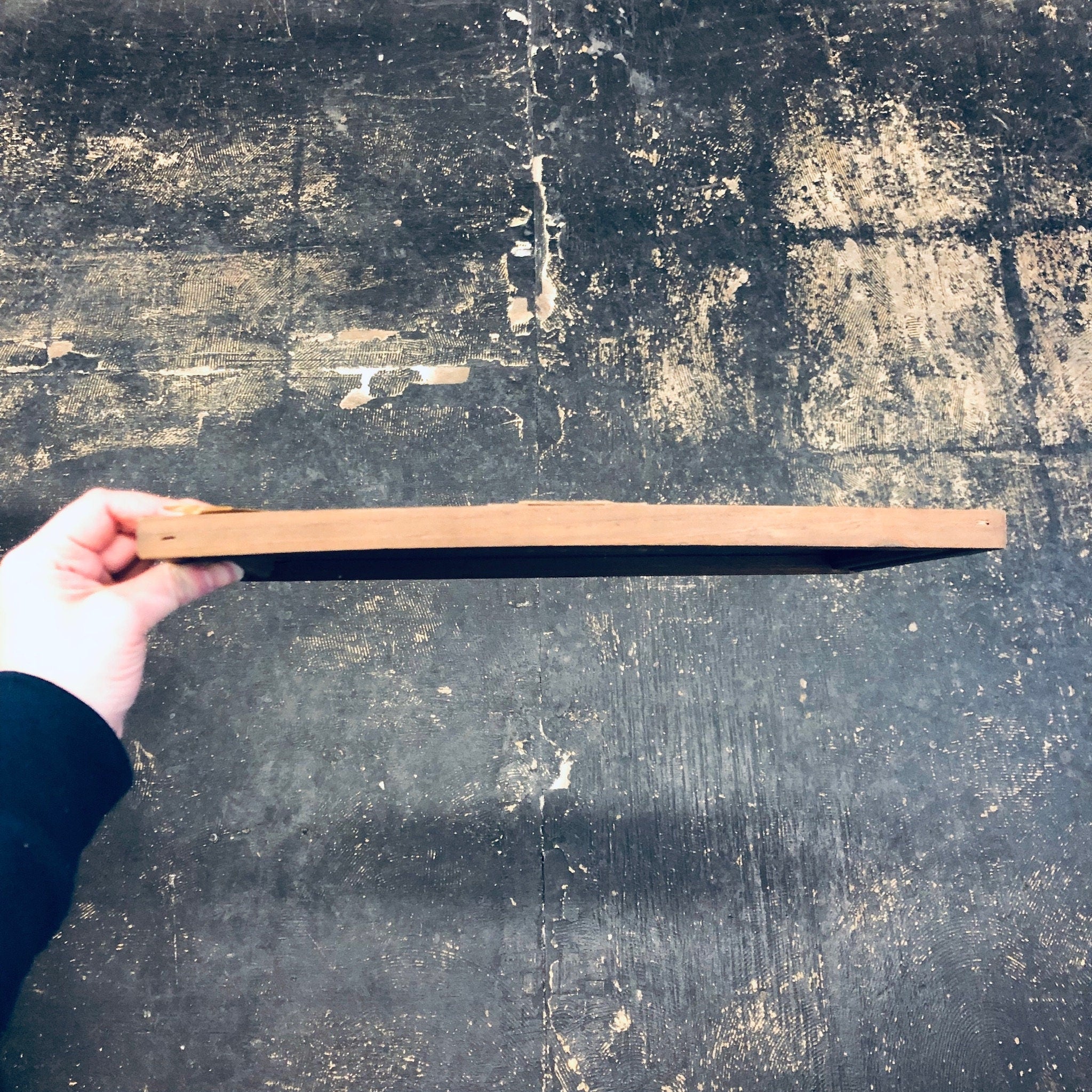 Hand holding a wooden ruler on a grungy, weathered concrete surface
