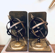 Pair of vintage brass armillary sphere bookends with Roman numeral dials on antique metal bases, unique library or bookshelf decor