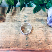 Vintage silver swirl band ring on rustic wooden surface with greenery in background