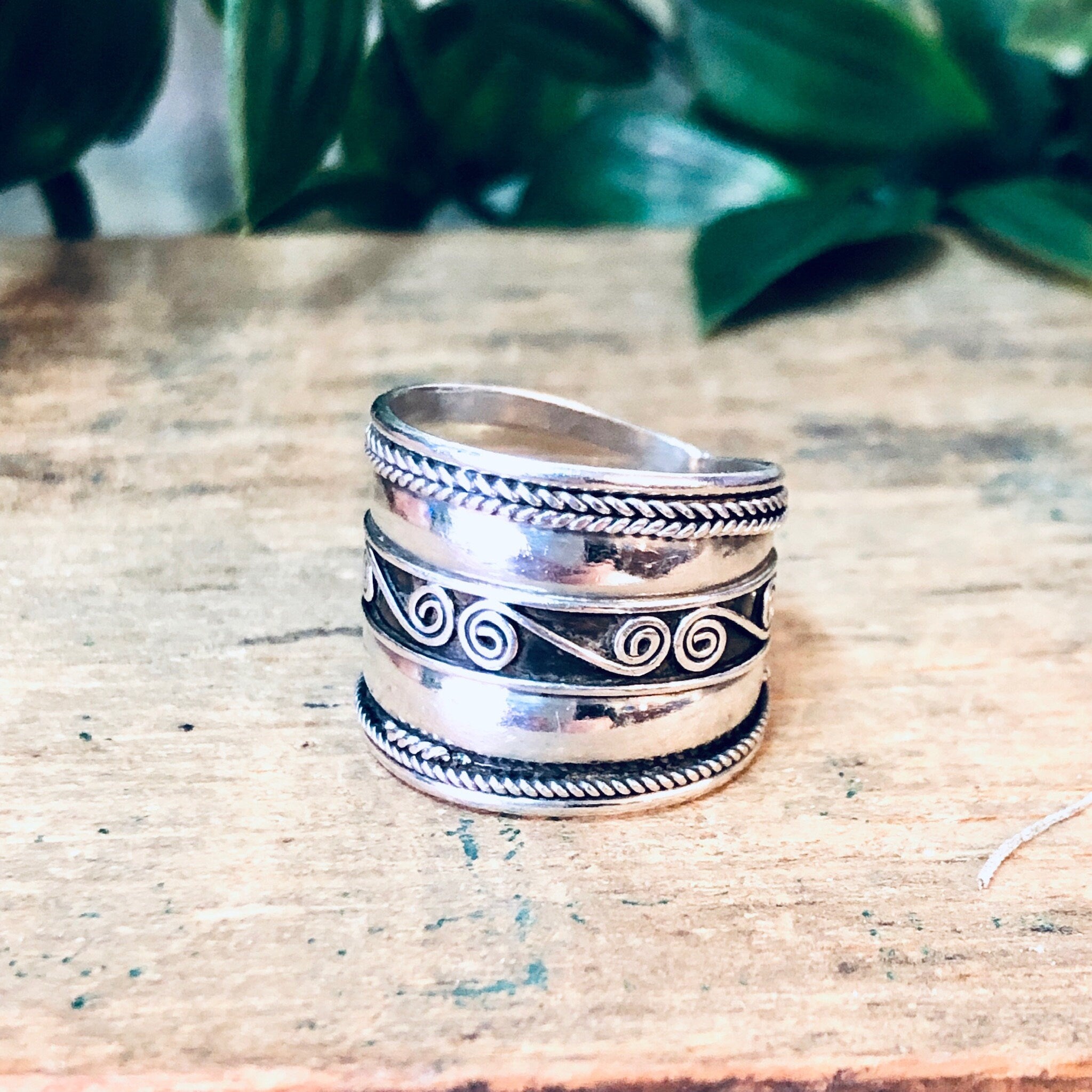 Vintage silver swirl design band ring on rustic wooden surface with green plant in background