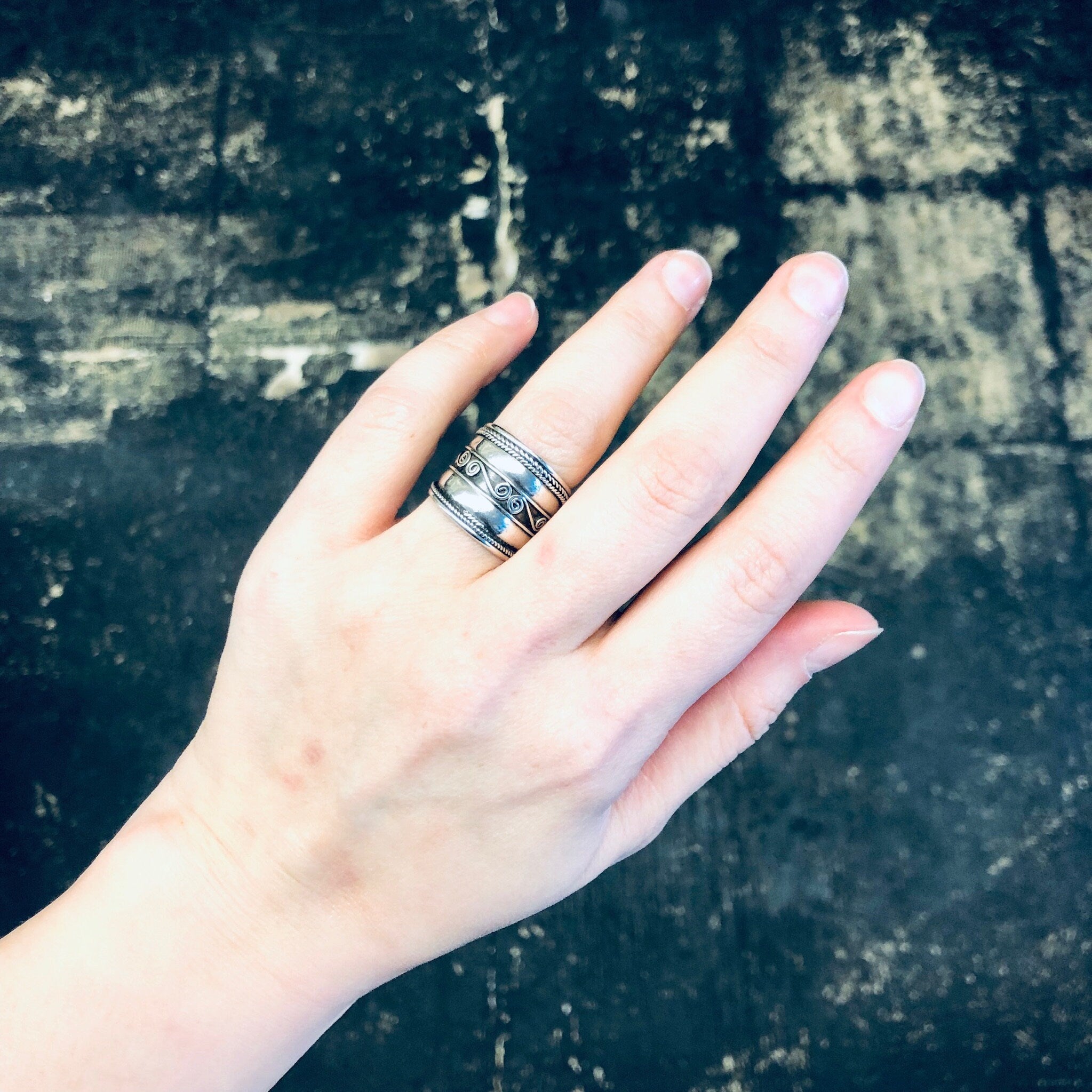 Vintage silver swirl design band ring on hand against textured background