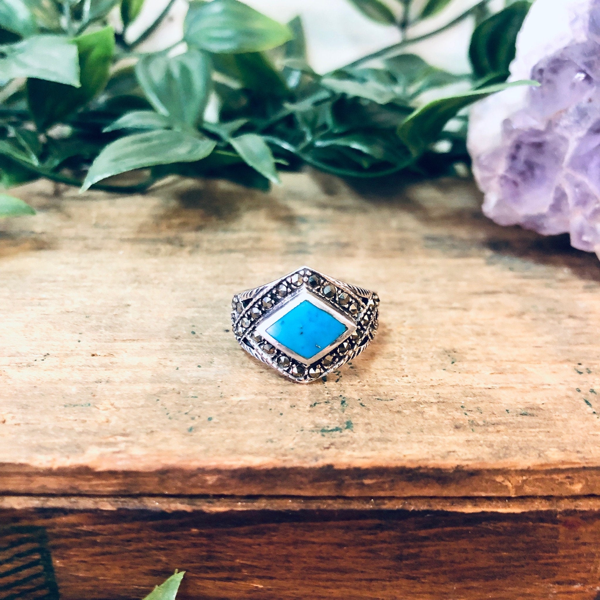 Vintage 925 silver marcasite ring with turquoise stone, diamond-shaped sparkly statement jewelry on wooden surface with greenery background.