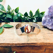 Vintage silver cuff bracelet with red natural stone on wooden surface surrounded by amethyst crystals and greenery.