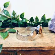 Vintage silver cuff bracelet with red natural stone on wooden surface surrounded by green leaves
