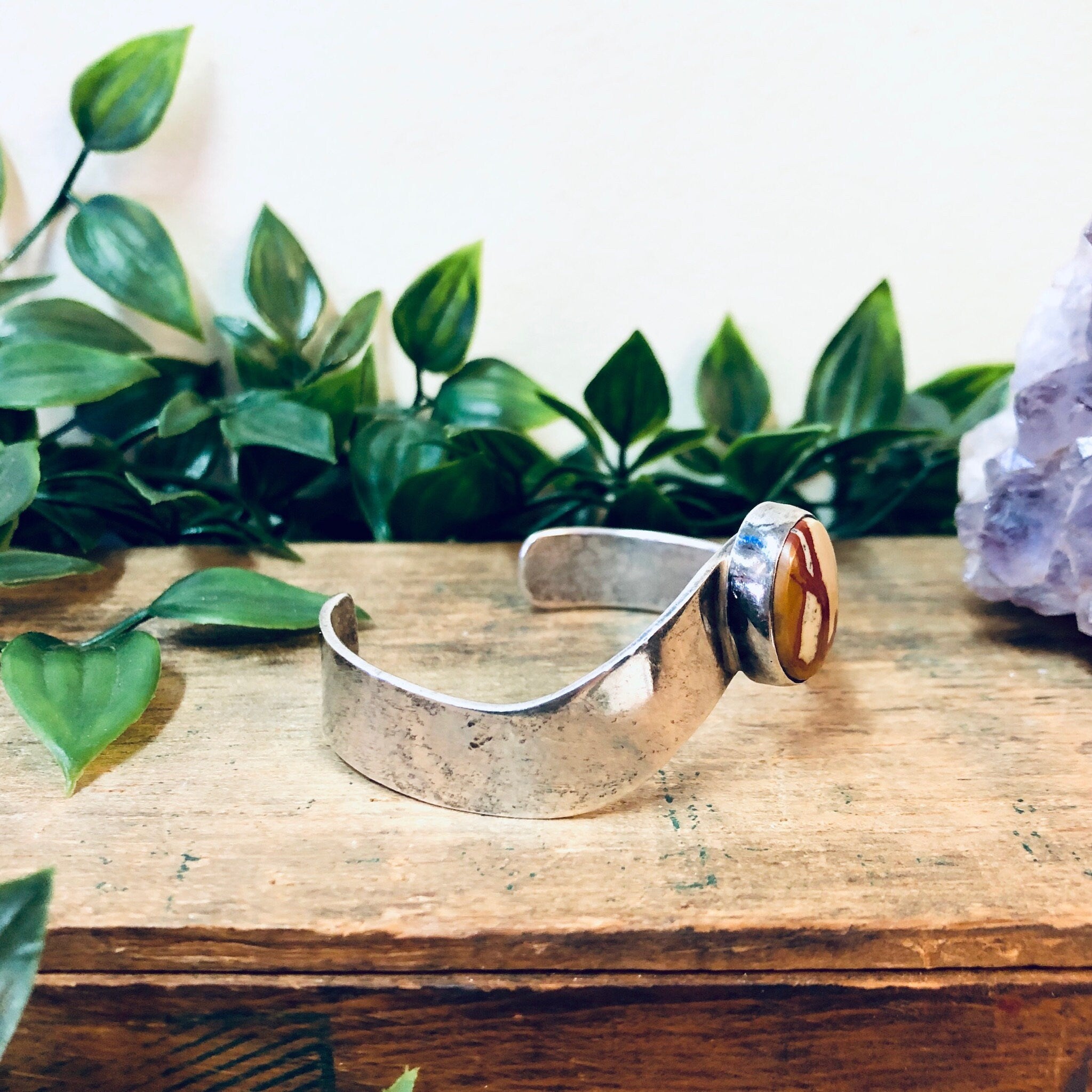 Vintage silver cuff bracelet with red natural stone on wooden surface surrounded by green leaves