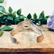 Vintage silver cuff bracelet with natural red stone on wooden surface with green foliage in background