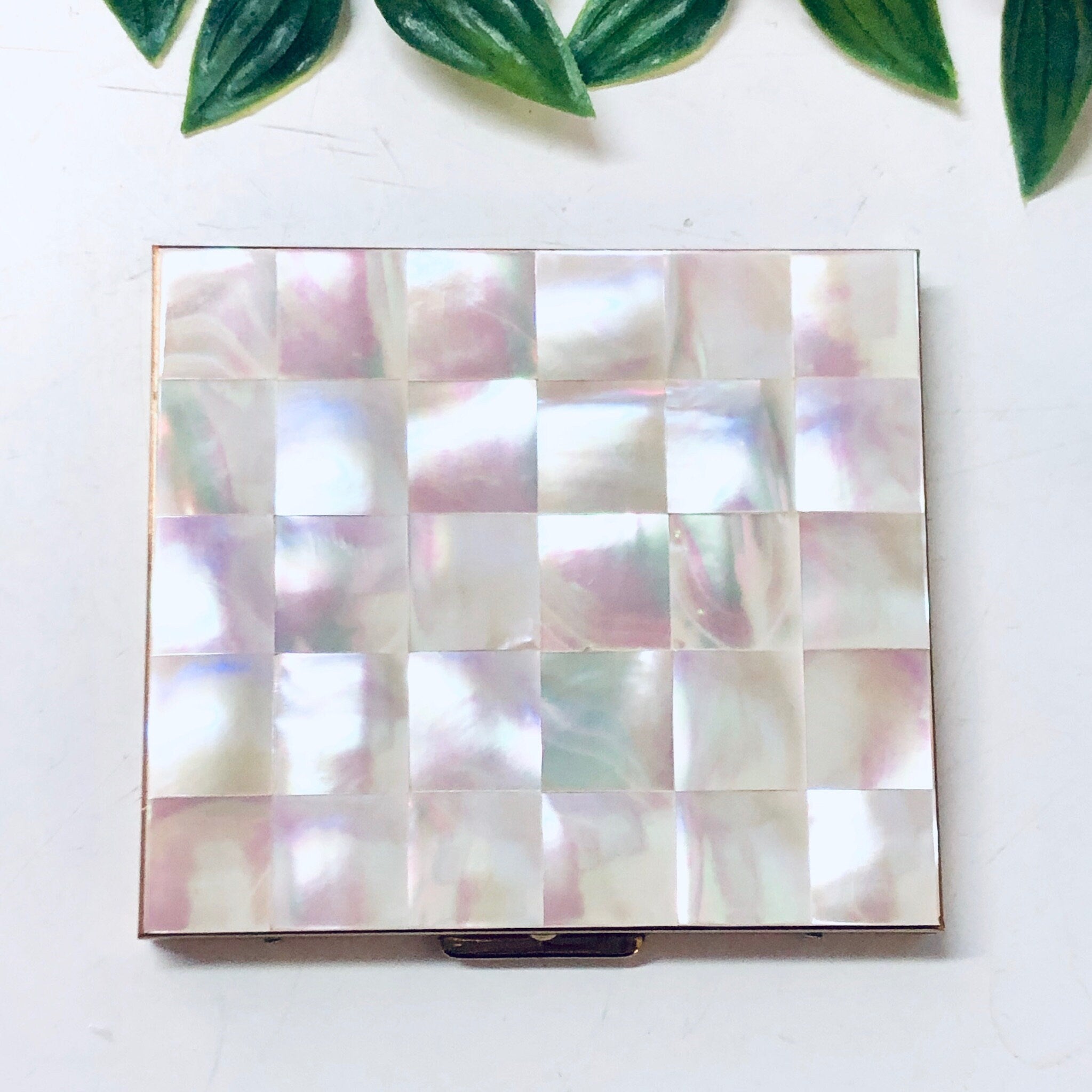 Vintage mother of pearl cigarette case or business card holder from Bailey Banks and Biddle, featuring a checkered pink mosaic design, displayed with green leaves above on a white background.